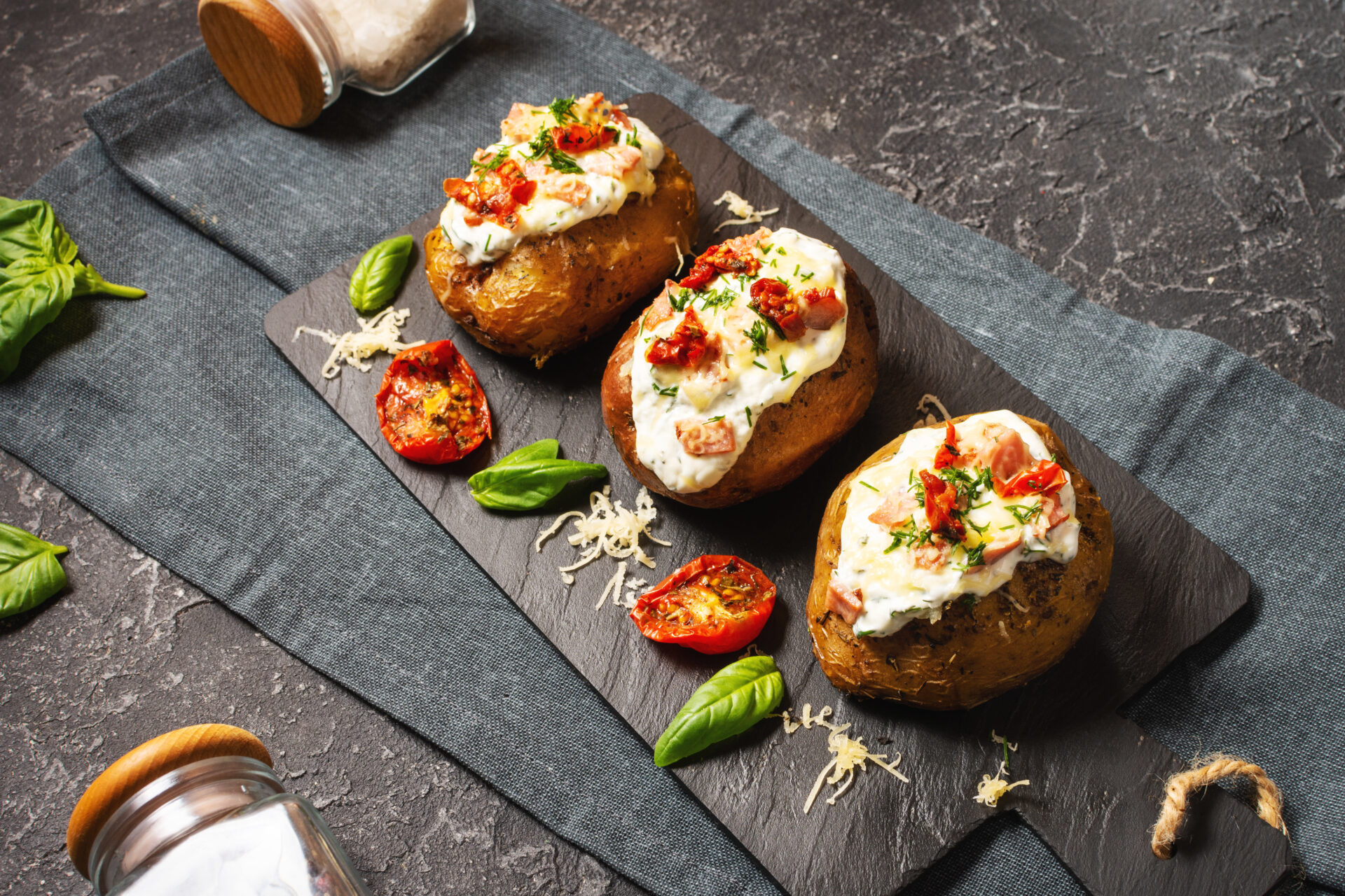 Baked stuffed potatoes with bacon, tomato and cheese on stone background.